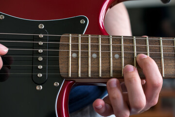 Close up view of a hand pressing the strings on an electric guitar, near the neck joint.