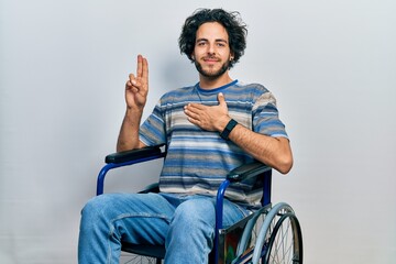 Handsome hispanic man sitting on wheelchair smiling swearing with hand on chest and fingers up,...