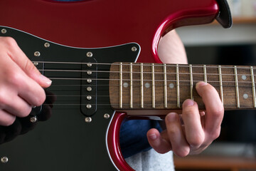 Close up view of a hand pressing the strings on an electric guitar, near the neck joint.