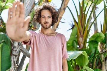 Young hispanic man outdoors on a sunny day with open hand doing stop sign with serious and...