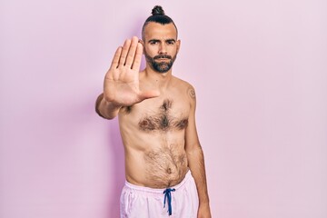 Fototapeta premium Young hispanic man shirtless wearing swimsuit doing stop sing with palm of the hand. warning expression with negative and serious gesture on the face.