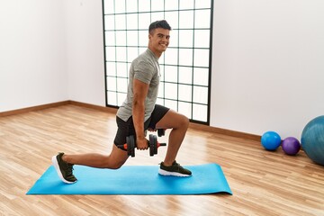 Young hispanic man smiling confident training using dumbbells at sport center