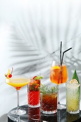 set cocktails on marble table and light background. five kinds of colorful summer cocktails in glasses and shadow of tropic leaf on background. Mojito, Aperol Spritz, margarita