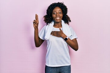 Young african american woman wearing sportswear and towel smiling swearing with hand on chest and...