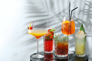 set cocktails on marble table and light background. five kinds of colorful summer cocktails in glasses and shadow of tropic leaf. Mojito, Aperol Spritz, margarita