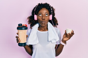 Young african american woman wearing sport clothes drinking a protein shake making fish face with...