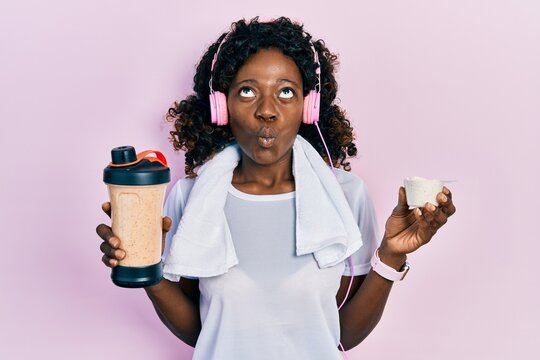 Young african american woman wearing sport clothes drinking a protein shake making fish face with mouth and squinting eyes, crazy and comical.