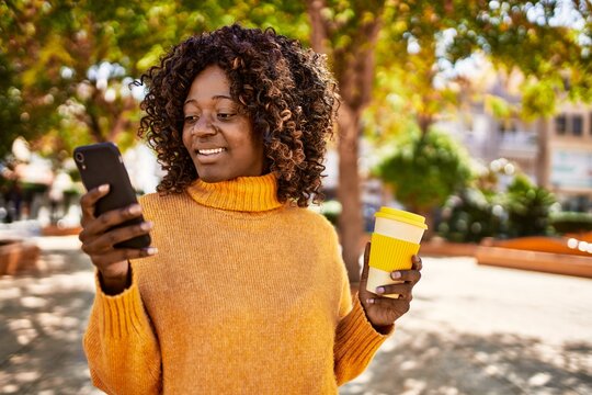 African american woman using smartphone drinking coffee at park