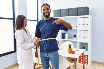 Dietitian at the clinic using tape measure measuring waist of client pointing finger to one self...