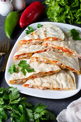Mexican snack quesadilla from tortilla with bacon, chicken, cheese and pepper in white plate on dark gray background