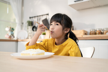 Portrait of Asian happy young kid girl eating cake in kitchen at home. 