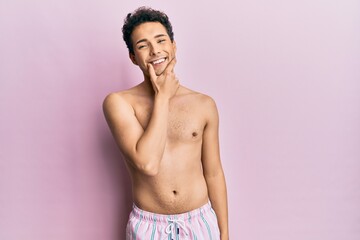 Young handsome man wearing swimwear shirtless looking confident at the camera smiling with crossed arms and hand raised on chin. thinking positive.