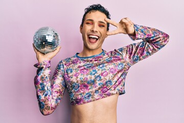 Handsome man wearing make up holding shiny disco ball smiling and laughing hard out loud because...