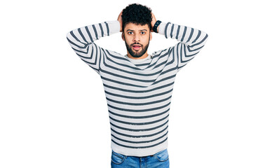 Young arab man with beard wearing casual striped sweater crazy and scared with hands on head, afraid and surprised of shock with open mouth