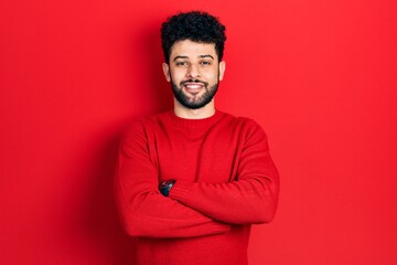 Obraz premium Young arab man with beard wearing casual red sweater happy face smiling with crossed arms looking at the camera. positive person.