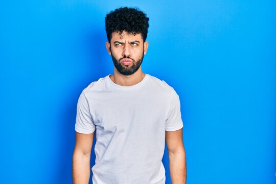 Young arab man with beard wearing casual white t shirt making fish face with lips, crazy and comical gesture. funny expression.