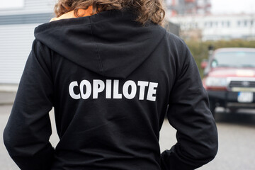 Closeup of girl wearing a black printed sweat shirt with text in french :  copilote, traduction in...