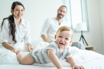 Caucasian parents play with cute baby boy child infant on bed at home.