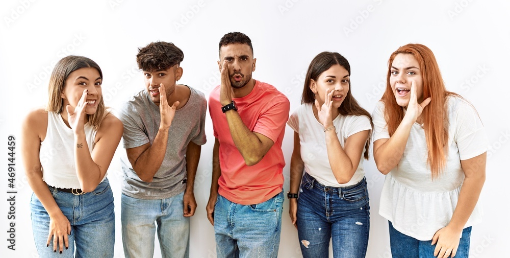 Poster group of young friends standing together over isolated background hand on mouth telling secret rumor