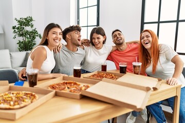 Group of young people smiling happy and hugging eating italian pizza at home.
