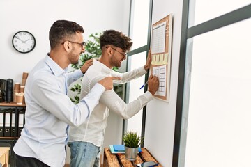 Fototapeta premium Two hispanic men couple writing on corkboard working at office