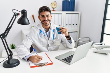 Handsome hispanic man working as doctor drinking a coffee at medical consultation