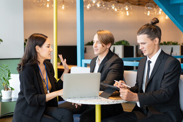 A group of business people, Asian businesswoman and Caucasian businessmen, sitting at a round table with laptop and tablet, having a business conversation during the small conference in a coffee shop.