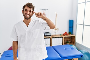 Young handsome physiotherapist man working at pain recovery clinic smiling pointing to head with one finger, great idea or thought, good memory