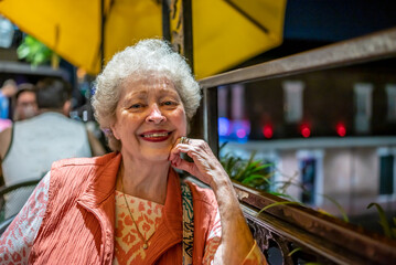 A beautiful senior woman enjoys dining on a balcony on Bourbon Street in the French Quarter at night, in New Orleans, Louisiana.