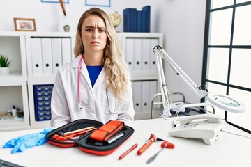 Young beautiful doctor woman with reflex hammer and medical instruments skeptic and nervous,...