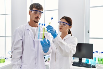 Man and woman partners wearing scientist uniform holding test tube at laboratory