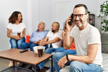 Group of middle age friends sitting on the sofa speaking. Man smiling happy talking on the smartphone at home.