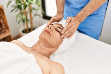 Fototapeta na wymiar Middle age man and woman wearing therapist uniform having facial massage session at beauty center
