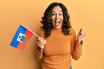 Middle age hispanic woman holding haiti flag screaming proud, celebrating victory and success very...