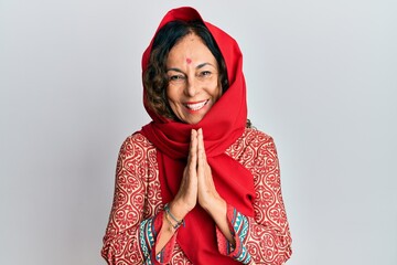 Middle age hispanic woman wearing tradition sherwani saree clothes praying with hands together...