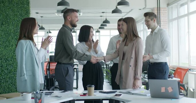people shaking hands at meeting while colleagues clapping and applauding. Group of young caucasian business people in formal wear, in modern white office. Success teamwork, partnership and handshake