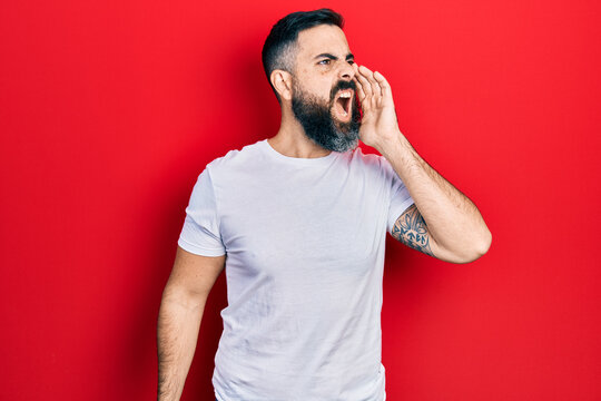 Young hispanic man wearing casual white t shirt shouting and screaming loud to side with hand on mouth. communication concept.