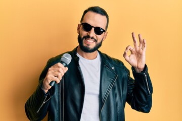 Young man with beard singing song using microphone doing ok sign with fingers, smiling friendly gesturing excellent symbol