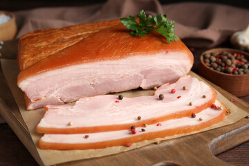 Delicious smoked bacon with parsley and pepper on wooden board, closeup