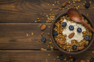 Top view of a clay cup with muesli and yogurt on a wooden table. Flat lay.