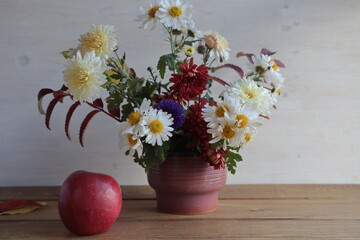 Autumn bouquet of chrysanthemums, chamomiles in a vase and an apple on the table.