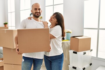 Fototapeta na wymiar Young hispanic couple smiling happy holding cardboard box at new home.