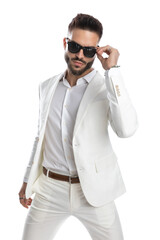 businessman arranging his sunglasses and wearing a white suit