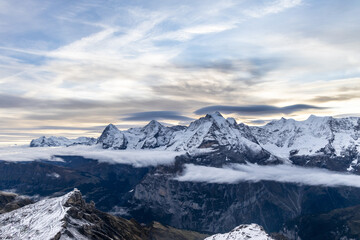 Naklejka na ściany i meble View of the famous peaks Jungfrau, Mönch and Eiger from the mountain Schilthorn in the Swiss Alps Switzerland at sunrise with dramatic clouds and fresh snow.