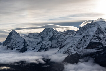 View of the famous peaks Jungfrau, Mönch and Eiger from the Schilthorn in the Swiss Alps Switzerland over the Lauterbrunnen Valley at sunrise with dramatic clouds and fresh snow. - obrazy, fototapety, plakaty