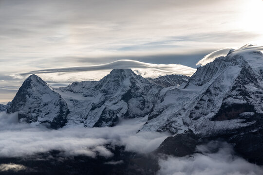 View of the famous peaks Jungfrau, Mönch and Eiger from the Schilthorn in the Swiss Alps Switzerland over the Lauterbrunnen Valley at sunrise with dramatic clouds and fresh snow.