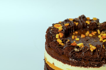 Close up part of chocolate cake with caramel and peanuts on green background.