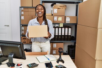 African woman working at small business ecommerce holding box smiling and laughing hard out loud...
