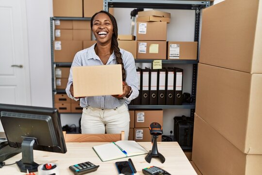 African woman working at small business ecommerce holding box smiling and laughing hard out loud because funny crazy joke.
