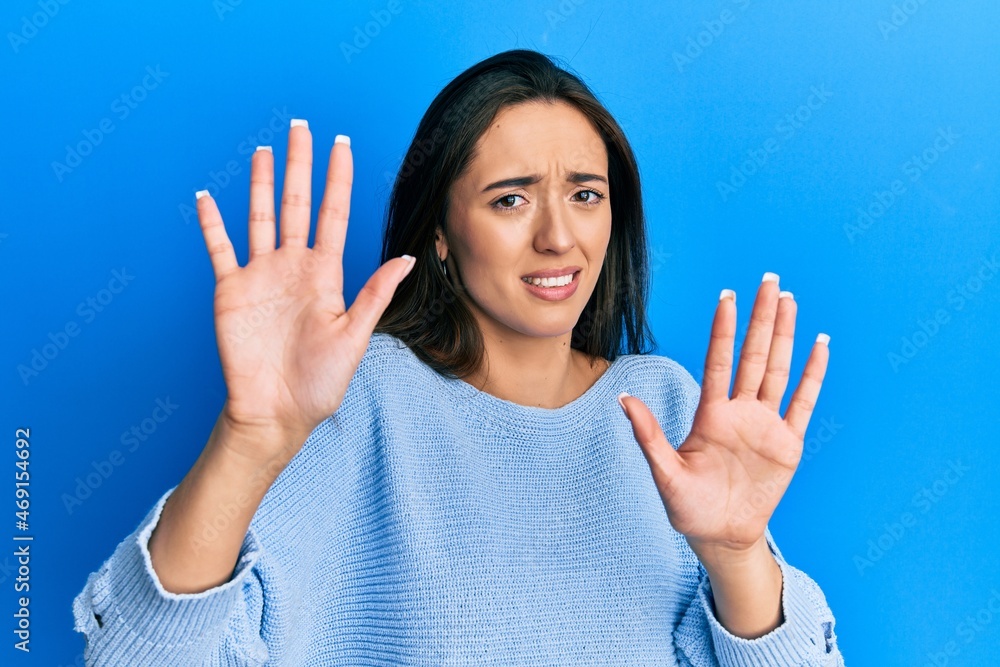 Sticker Young hispanic girl wearing casual clothes afraid and terrified with fear expression stop gesture with hands, shouting in shock. panic concept.